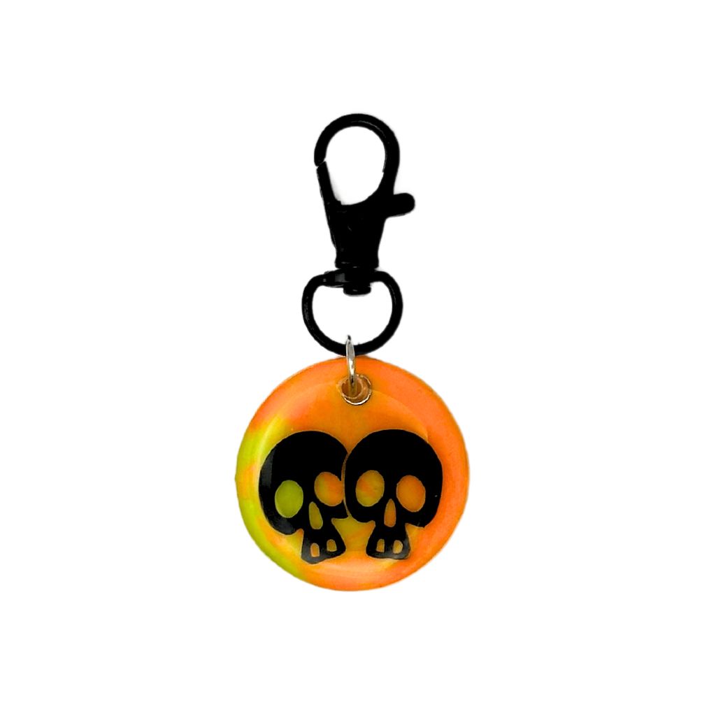 Round pet ID tag made of neon orange resin with two black skulls, featuring a customizable QR code and keychain clasp.