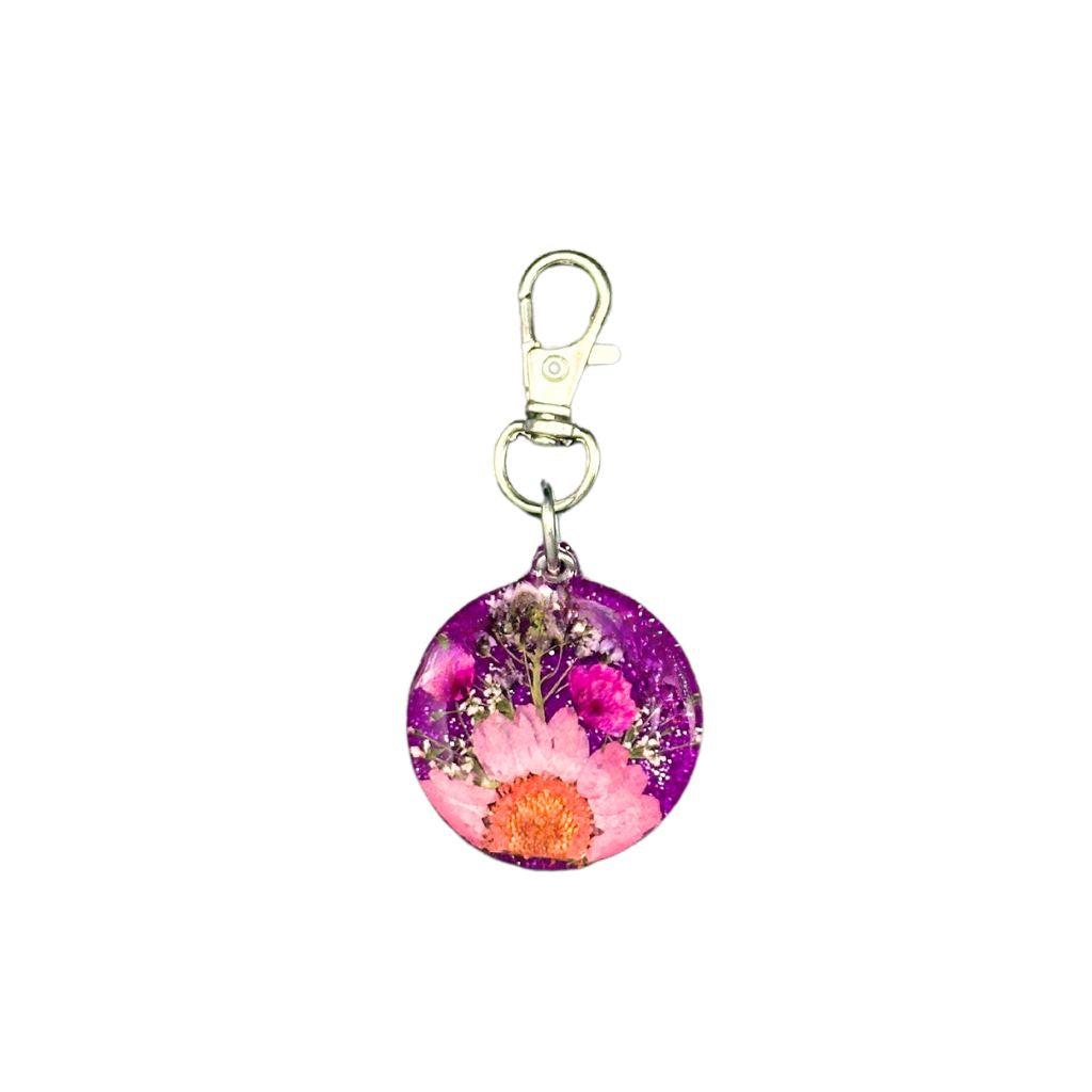Round pet ID tag made of purple resin with embedded pink and white flowers, featuring a customizable QR code and keychain clasp.